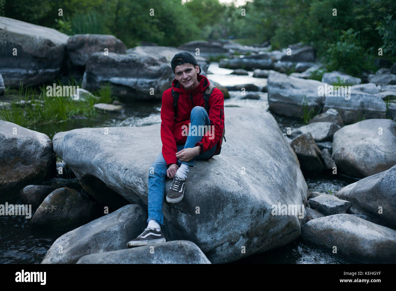 Uomo caucasico seduto sulla roccia nel fiume Foto Stock