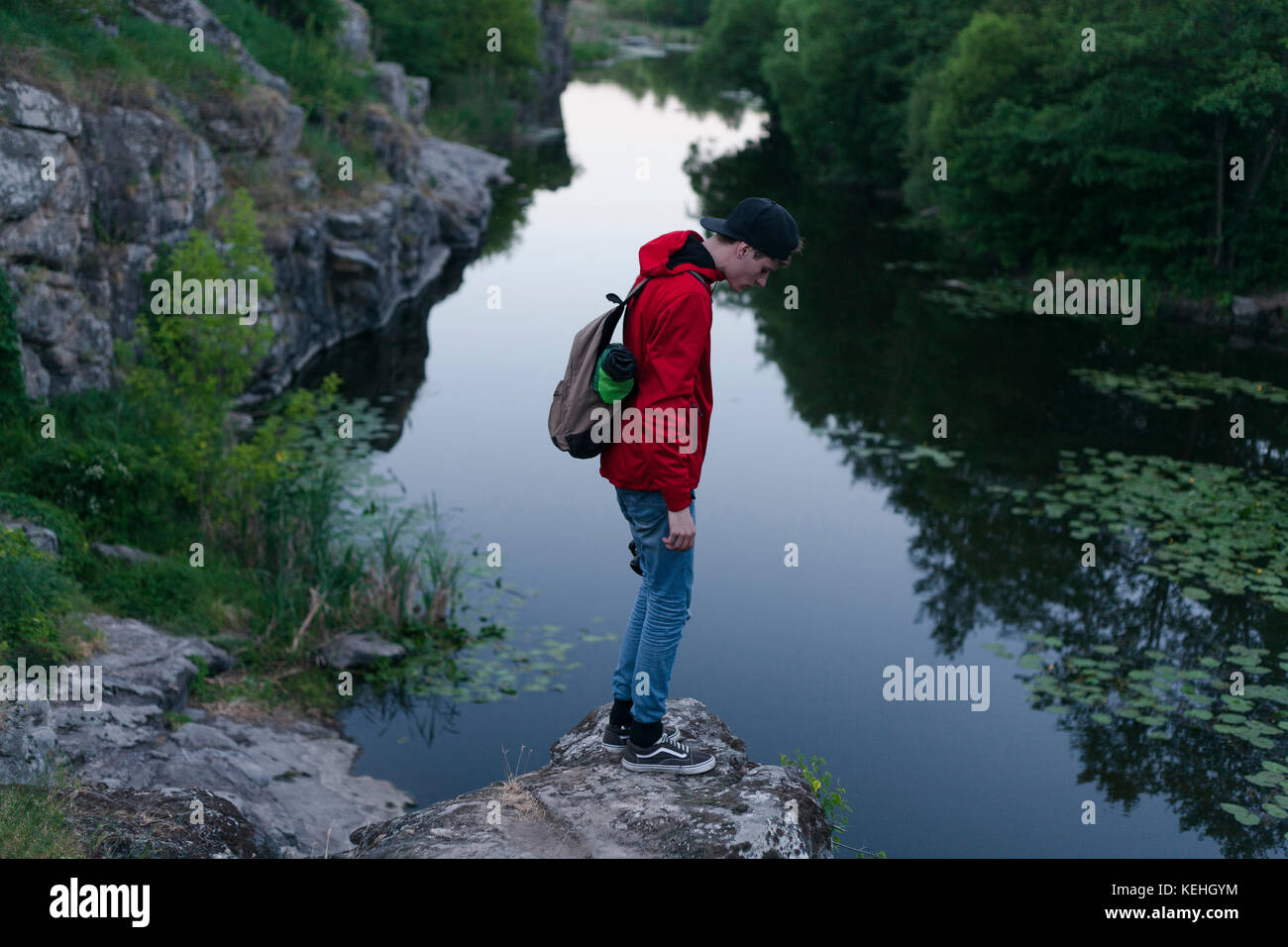 Uomo caucasico in piedi su roccia guardando giù al fiume Foto Stock