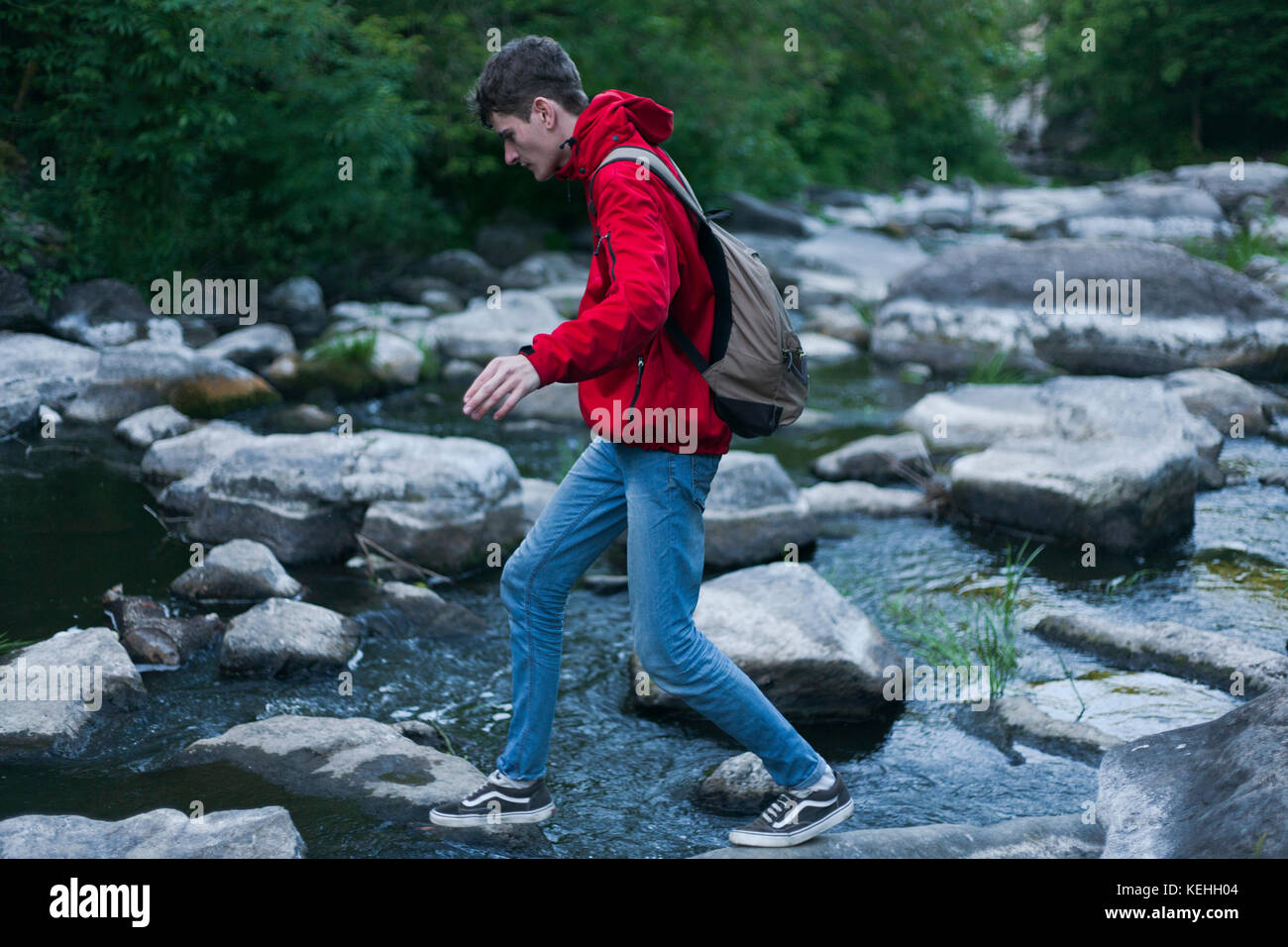 Uomo caucasico che cammina su rocce che attraversano il fiume Foto Stock