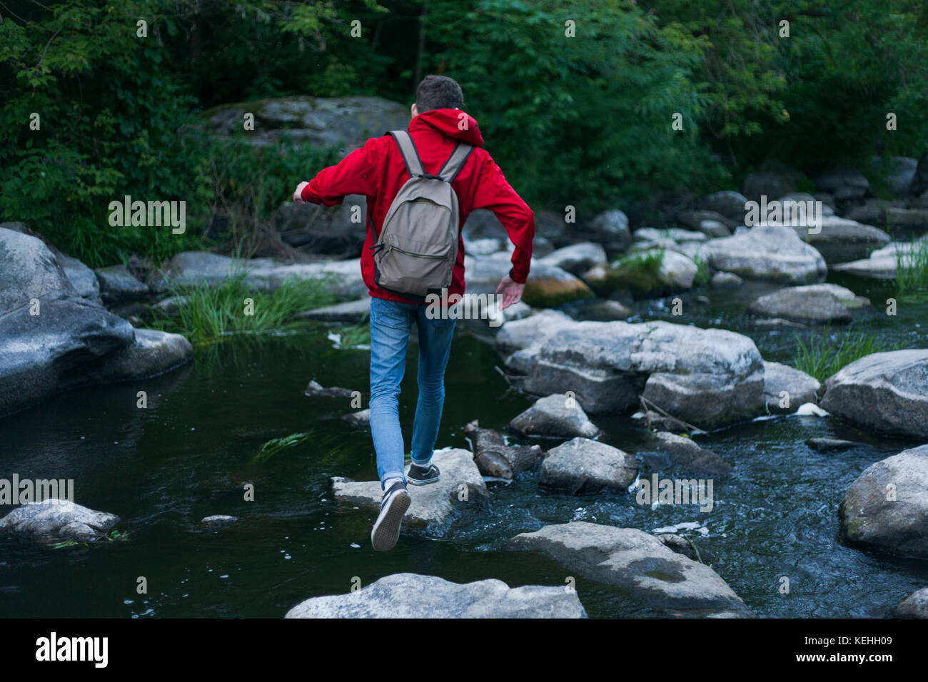 Uomo caucasico che cammina su rocce che attraversano il fiume Foto Stock