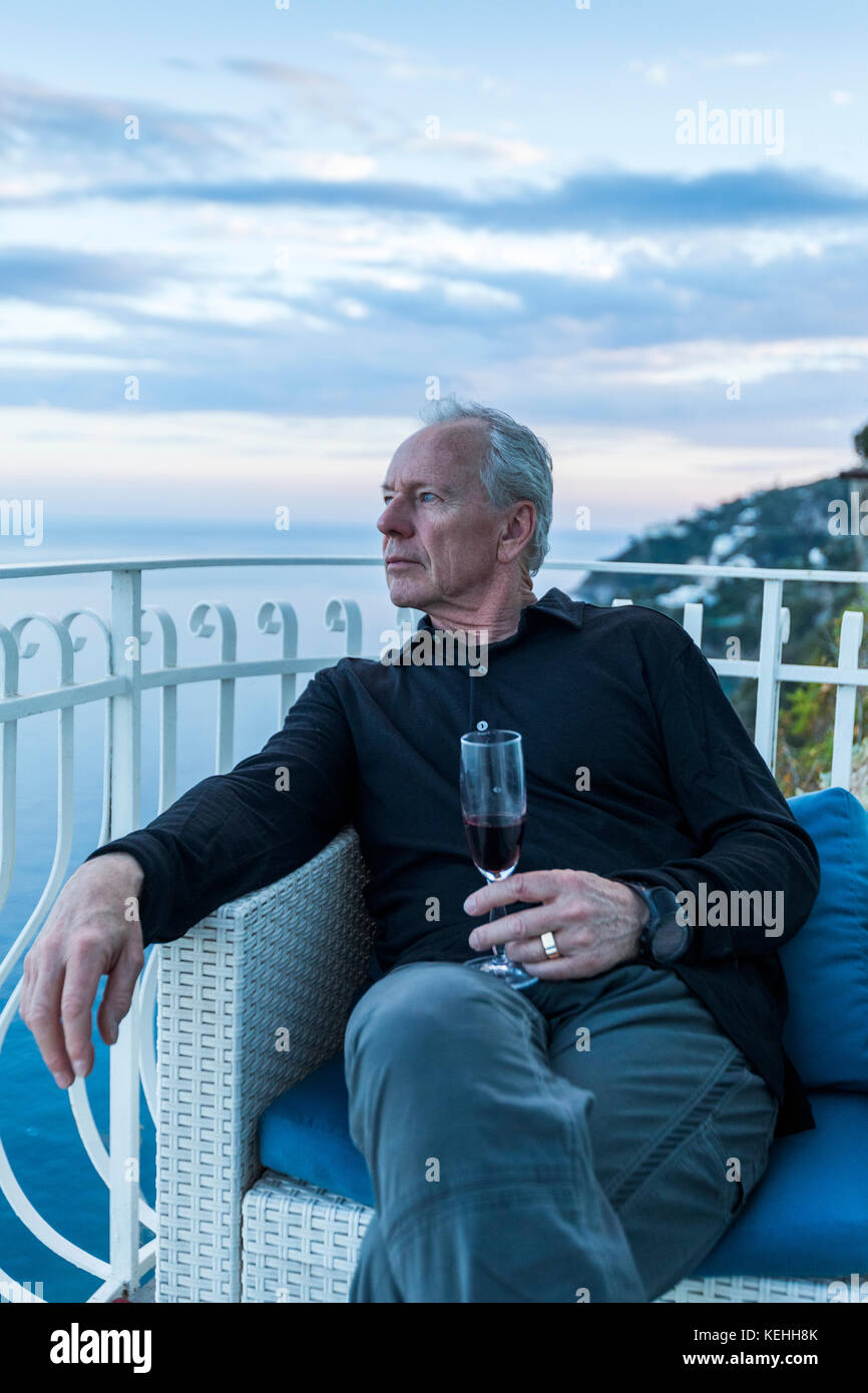 Uomo caucasico che beve vino sul balcone fronte mare Foto Stock