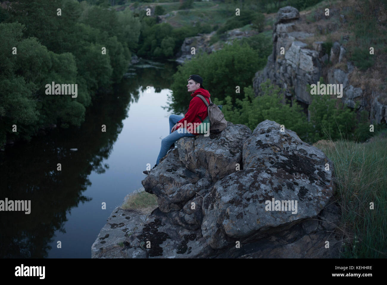 Uomo caucasico seduto su una roccia vicino al fiume Foto Stock
