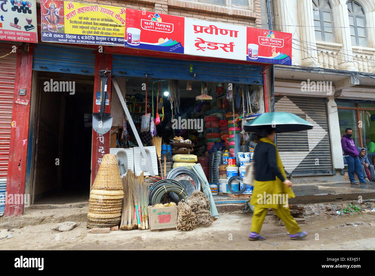 Pedonale femmina con un ombrello passando da un negozio di ferramenta in Kathmandu, Nepal. Foto Stock
