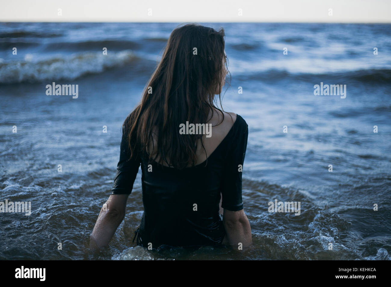 Donna caucasica che indossa abiti che guado in oceano Foto Stock