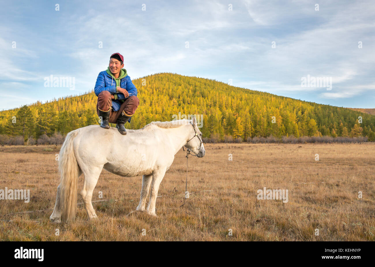 Il mongolo uomo seduto su un cavallo e fumare una sigaretta Foto Stock