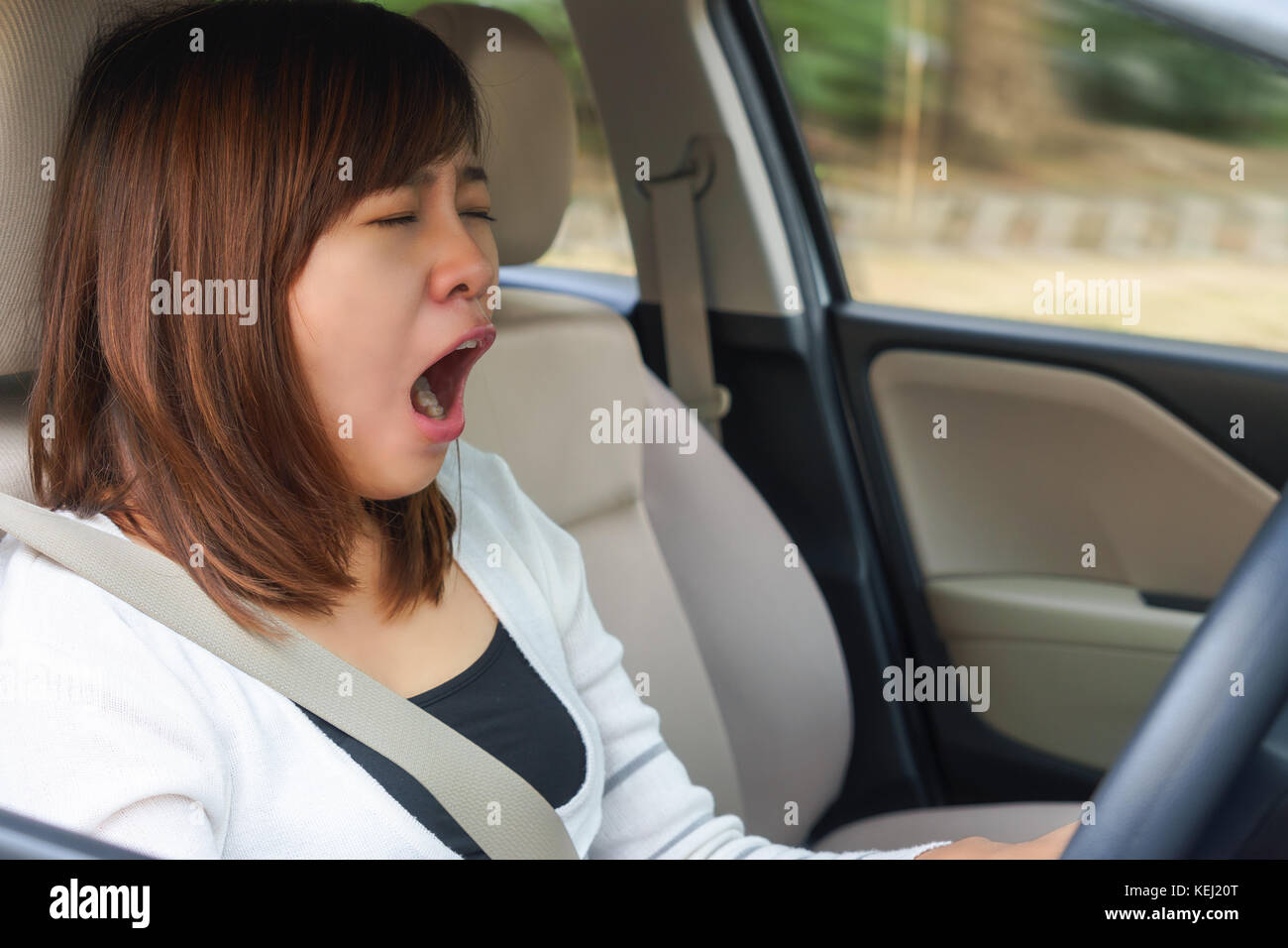 Closeup ritratto assonnato, sbadiglio, chiudere gli occhi giovane donna alla guida la sua auto dopo lunghe ore di viaggio, la privazione del sonno, concetto di incidente Foto Stock