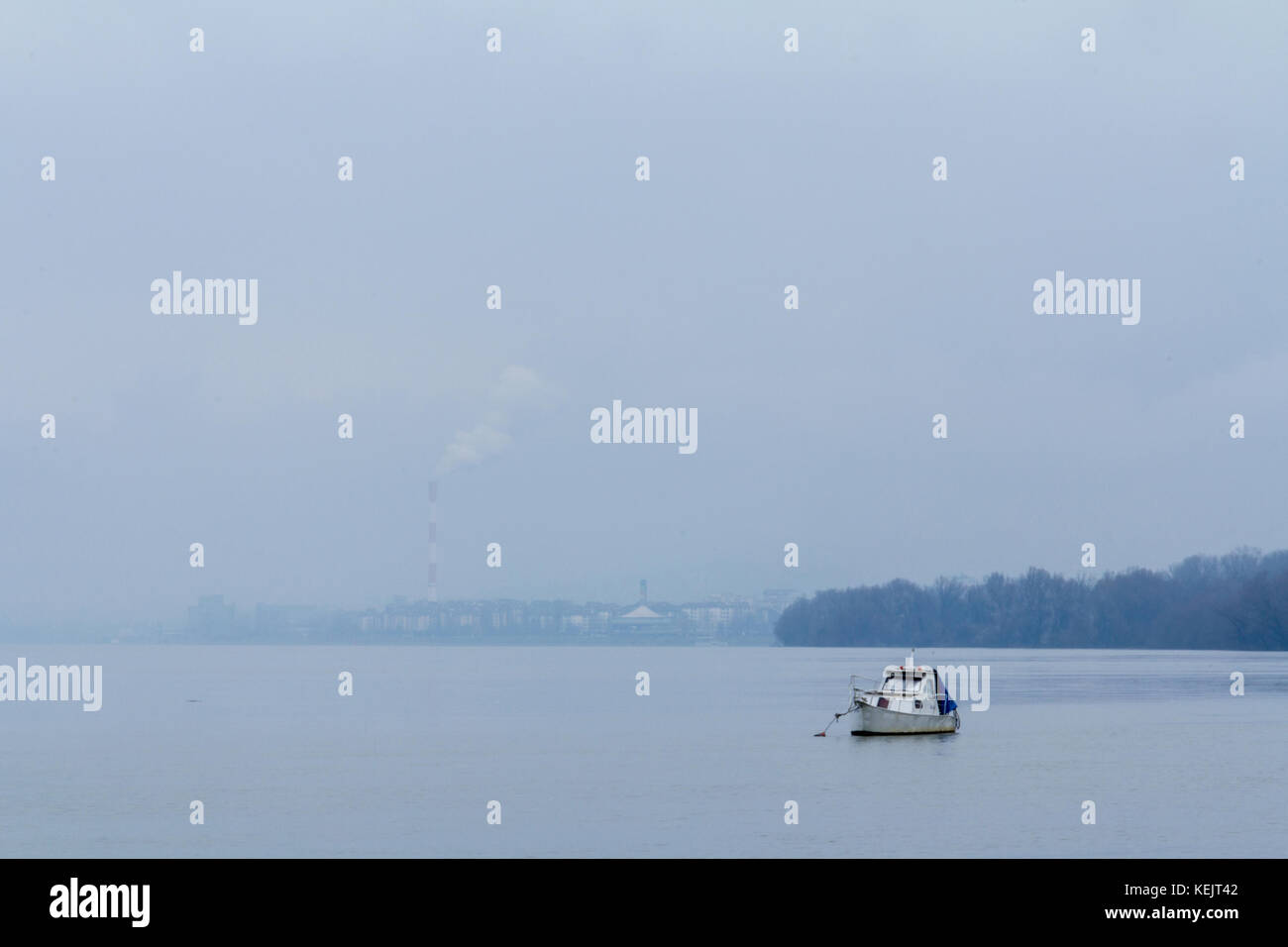 Belgrado sotto la nebbia visto da zemun, con una barca di fronte, sul fiume Danubio e i fumi di un camino industriale nell'immagine di sfondo o Foto Stock