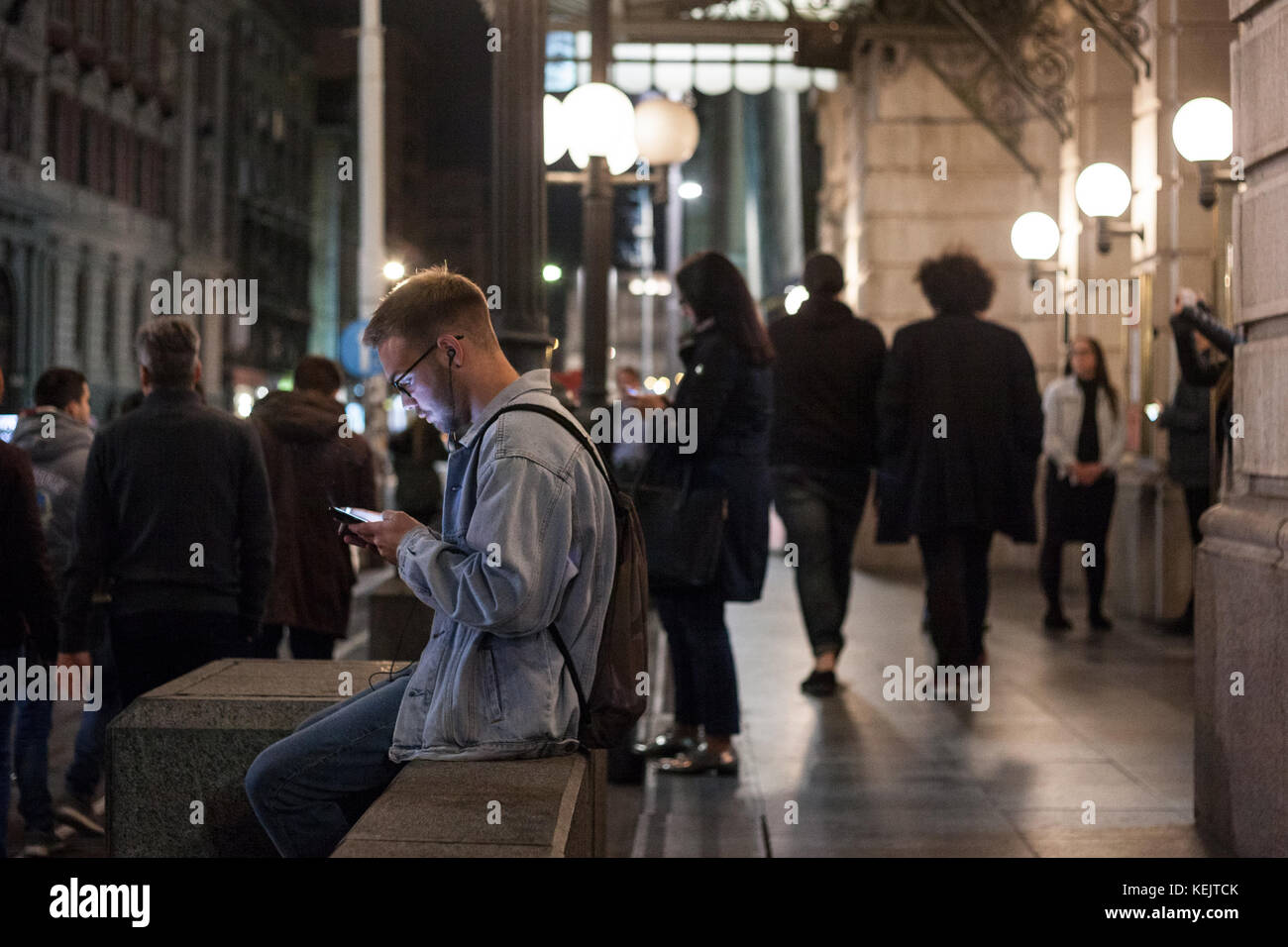 A Belgrado, in Serbia - ottobre 14, 201: giovane uomo bianco con il suo smartphone di notte a Belgrado, una donna facendo lo stesso in background. La Serbia è uno Foto Stock