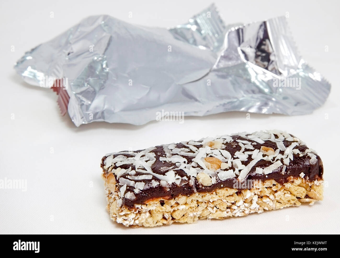 Granola bar e rabboccato con noce di cocco e cioccolato su sfondo bianco con un foglio di alluminio il confezionamento in background. focus sul primo piano granola bar. Foto Stock