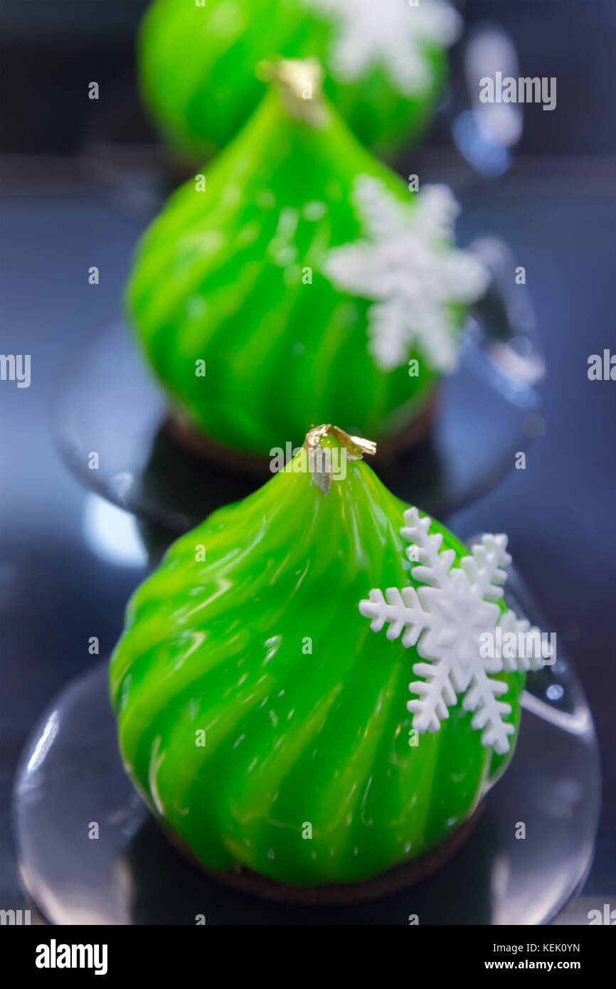Moderno mousse francese torta decorata in stile natalizio coperto con smalto verde specchio e il cioccolato bianco il simbolo del fiocco di neve. Foto Stock