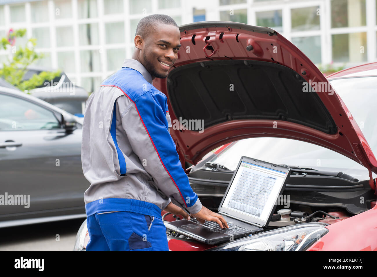 Giovani felici meccanico utilizzando laptop nella parte anteriore della vettura aperta motore Foto Stock