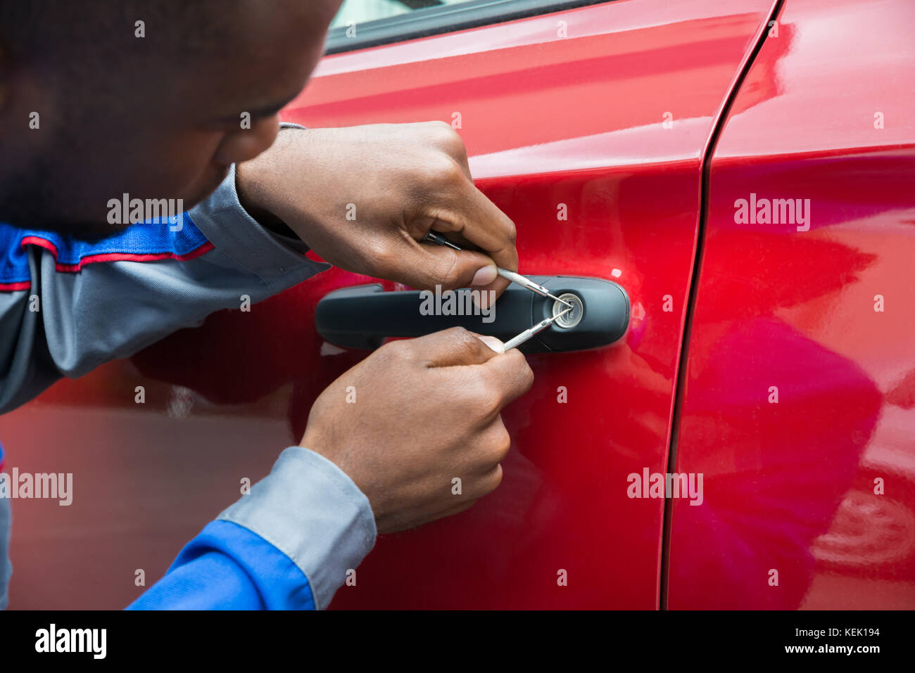 Giovane Maschio di contenimento meccanico Lockpicker per aprire auto rossa porta Foto Stock