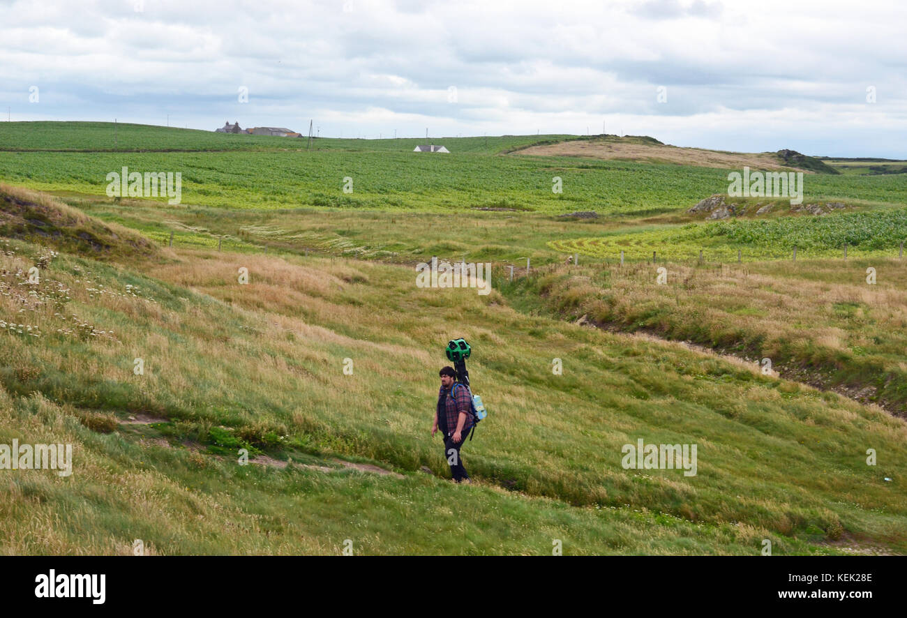 Uomo che cammina lungo la Anglesey sentiero costiero, con un grado di 360 fotocamera, scattare istantanee per Google Earth. Foto Stock