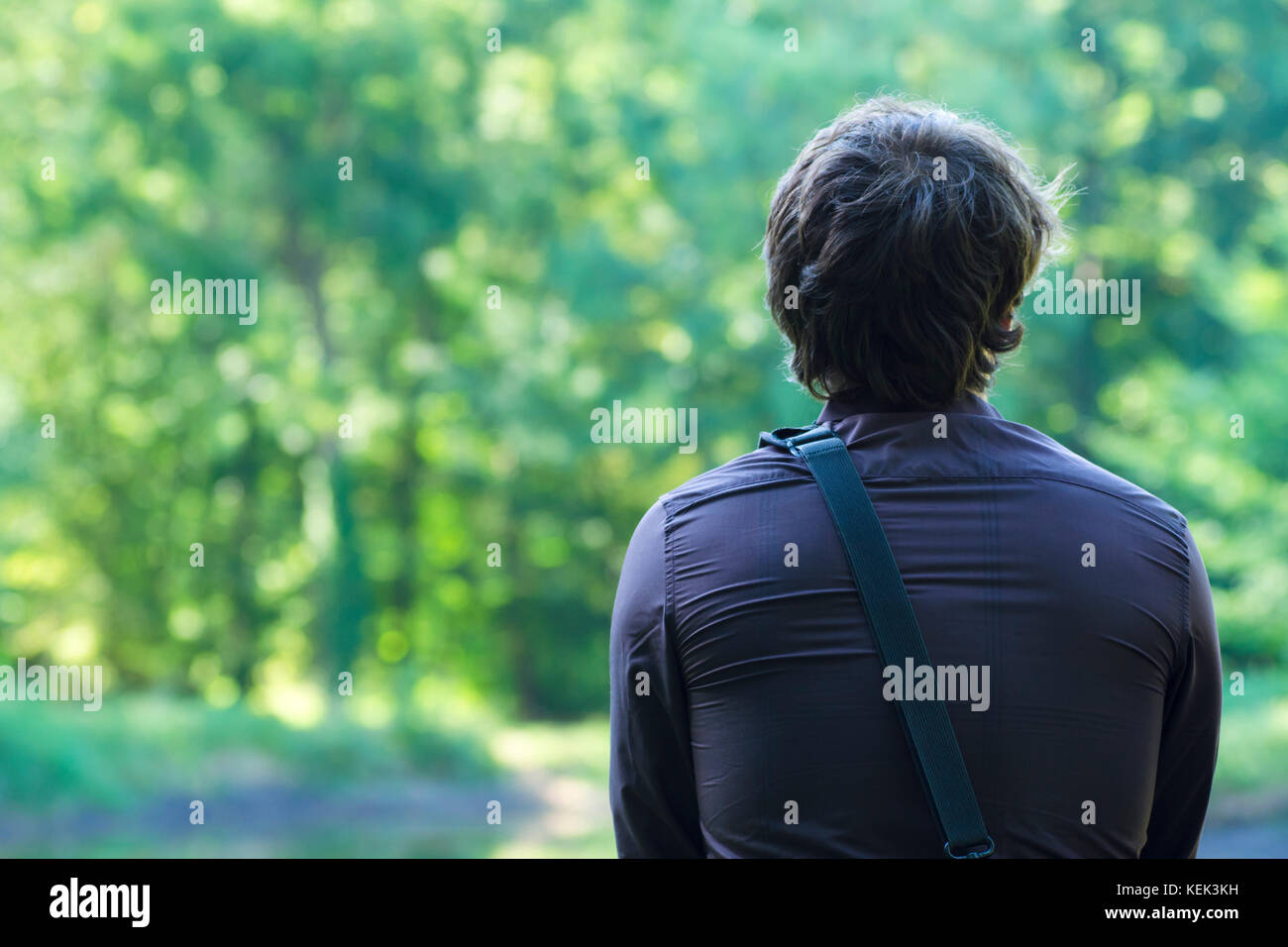 Una vista posteriore di un solitario giovane uomo seduto e guardando la natura con uno sfondo sfocato Foto Stock