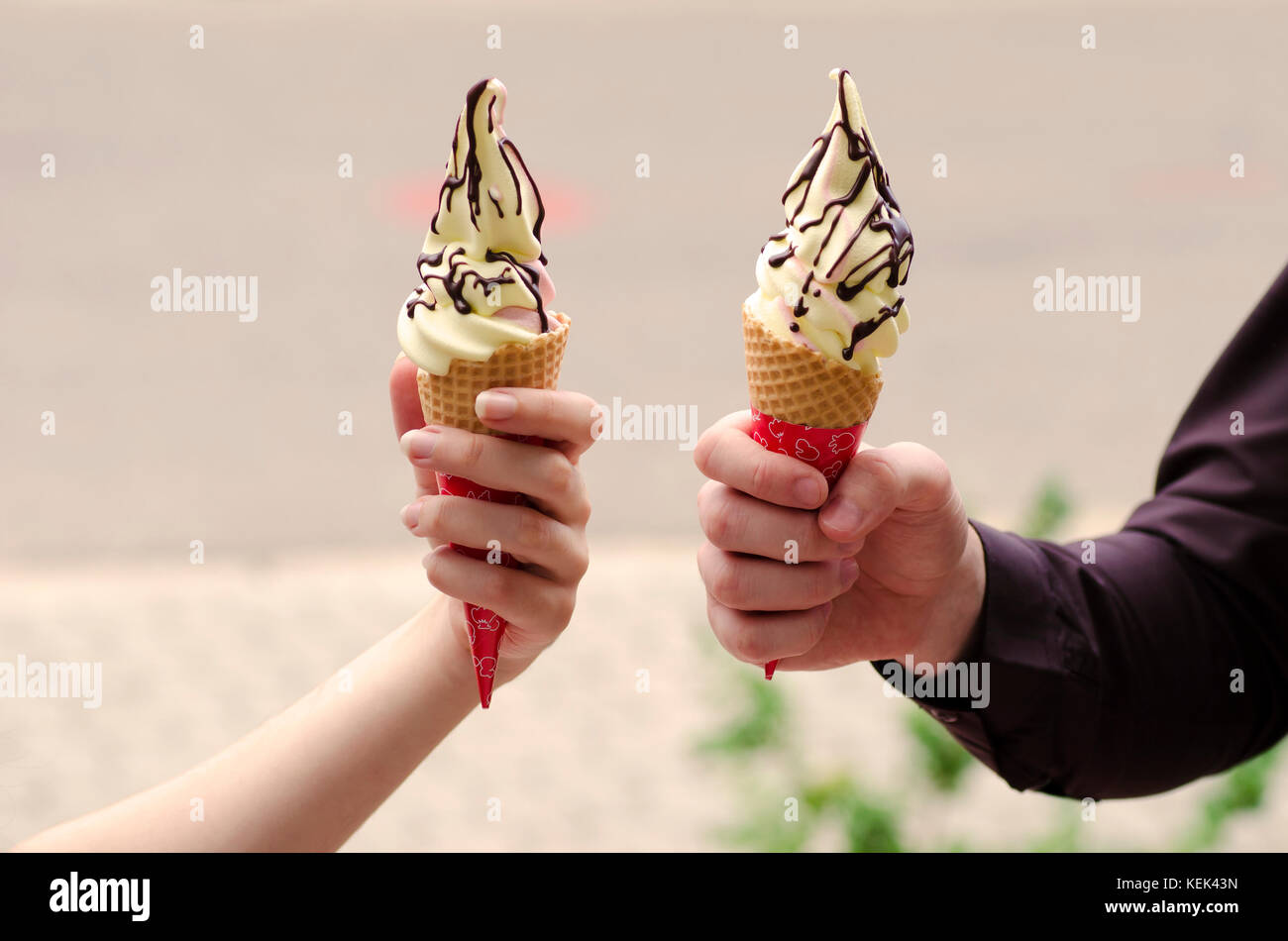 Vista ravvicinata delle mani di un ragazzo e una ragazza con due gelati con toping al cioccolato in una fetta con uno sfondo sfocato Foto Stock