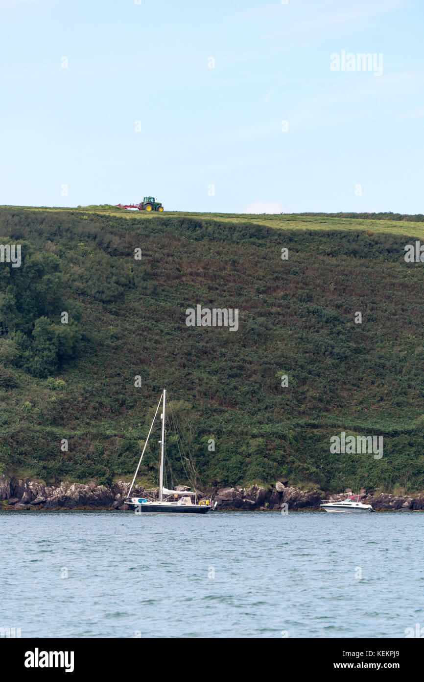Yacht ancorati nella baia di watwick con un trattore il taglio di erba sui campi sopra Foto Stock