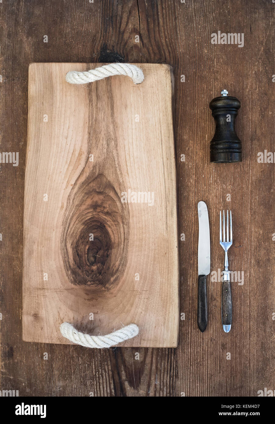 Cucina-ware set. vecchio rustico che serve il vassoio della scheda, il coltello e la forchetta, pepperbox su un vecchio sfondo di legno Foto Stock