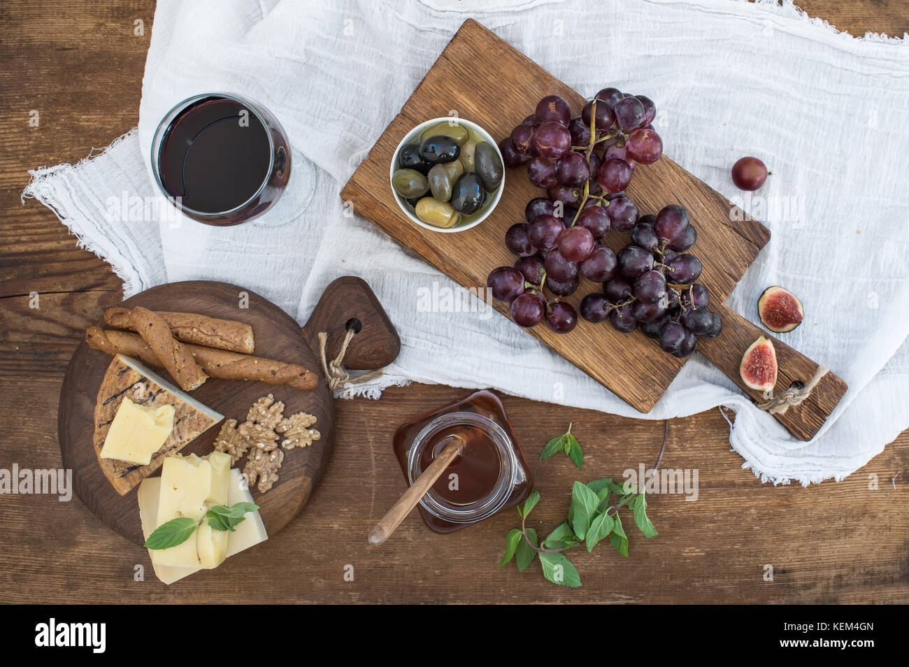 Bicchiere di vino rosso, formaggi, uva, noci, olive, miele e grissini sulla tavola in legno rustico Foto Stock