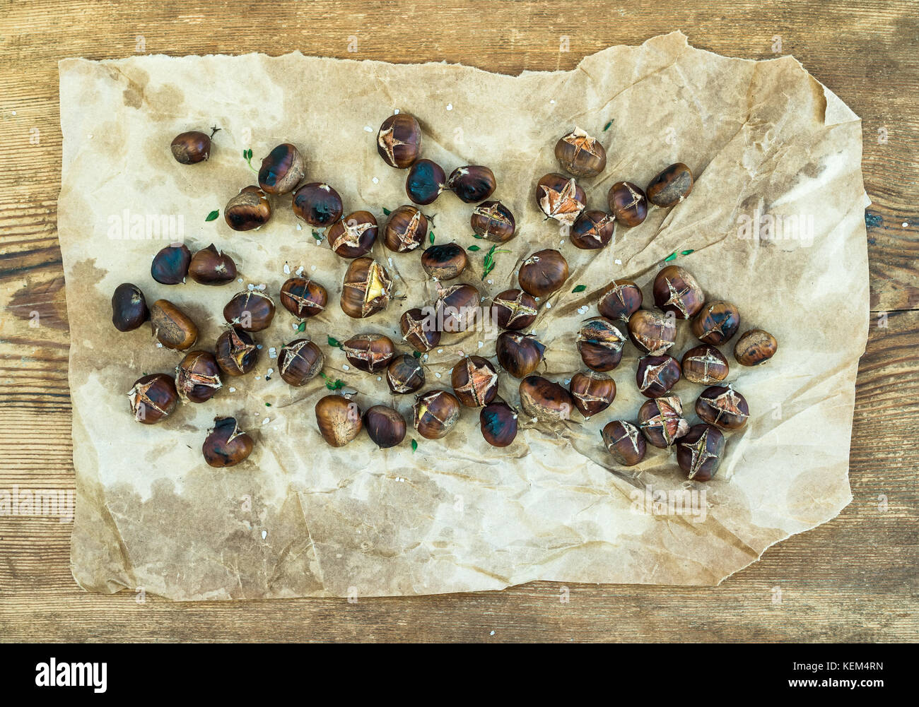 Castagne arrostite su usurato oleoso imbarcazioni carta su legno rustico sfondo, vista dall'alto. Foto Stock