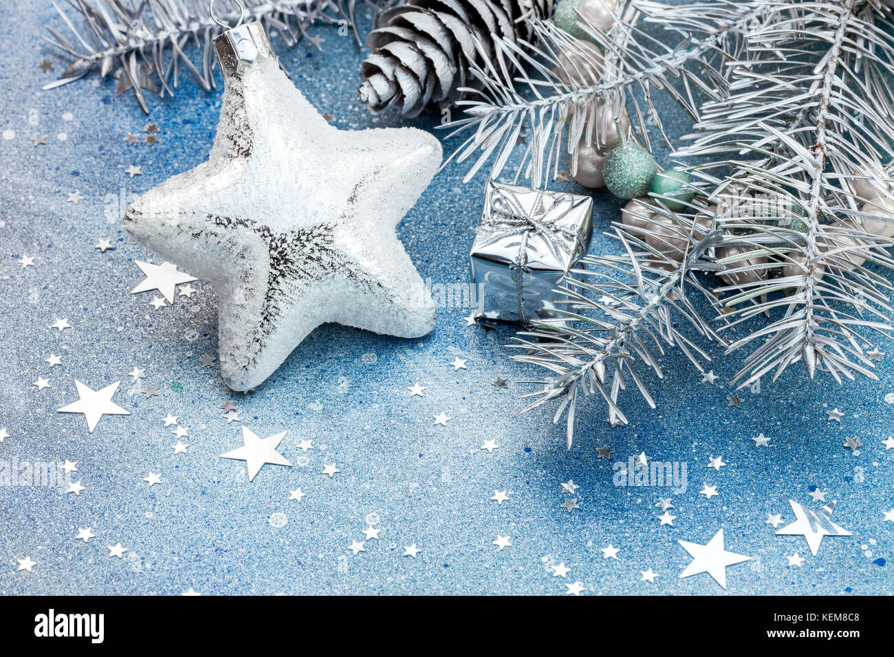Stella di vetro e piccola confezione regalo con argento ramo di abete e coni su blu scintillante sfondo con stelle Foto Stock