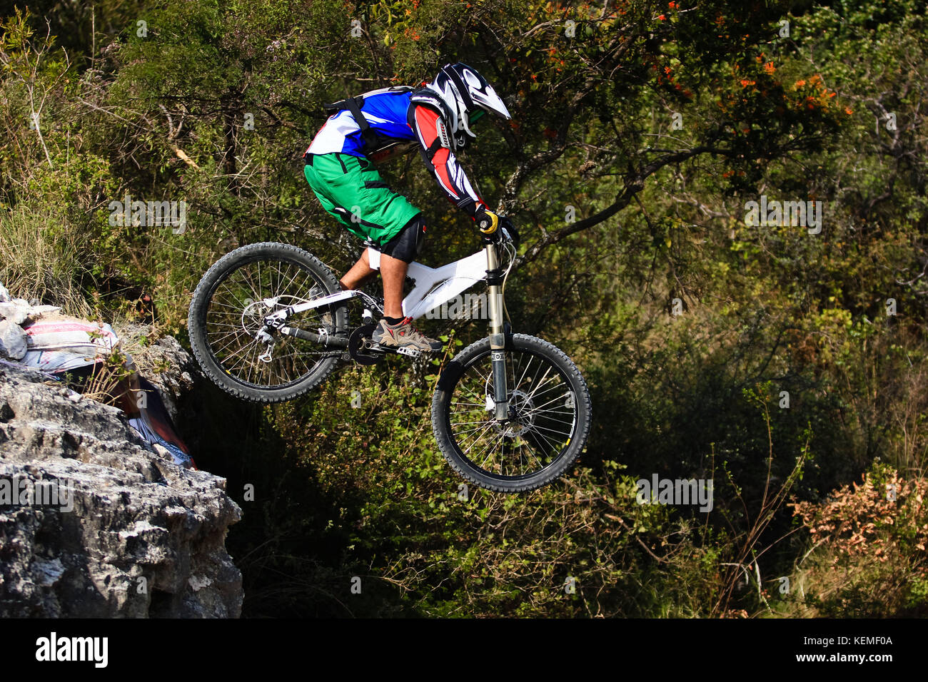 Downhill mountain biker con pantaloncini verde saltando da una caduta Foto Stock