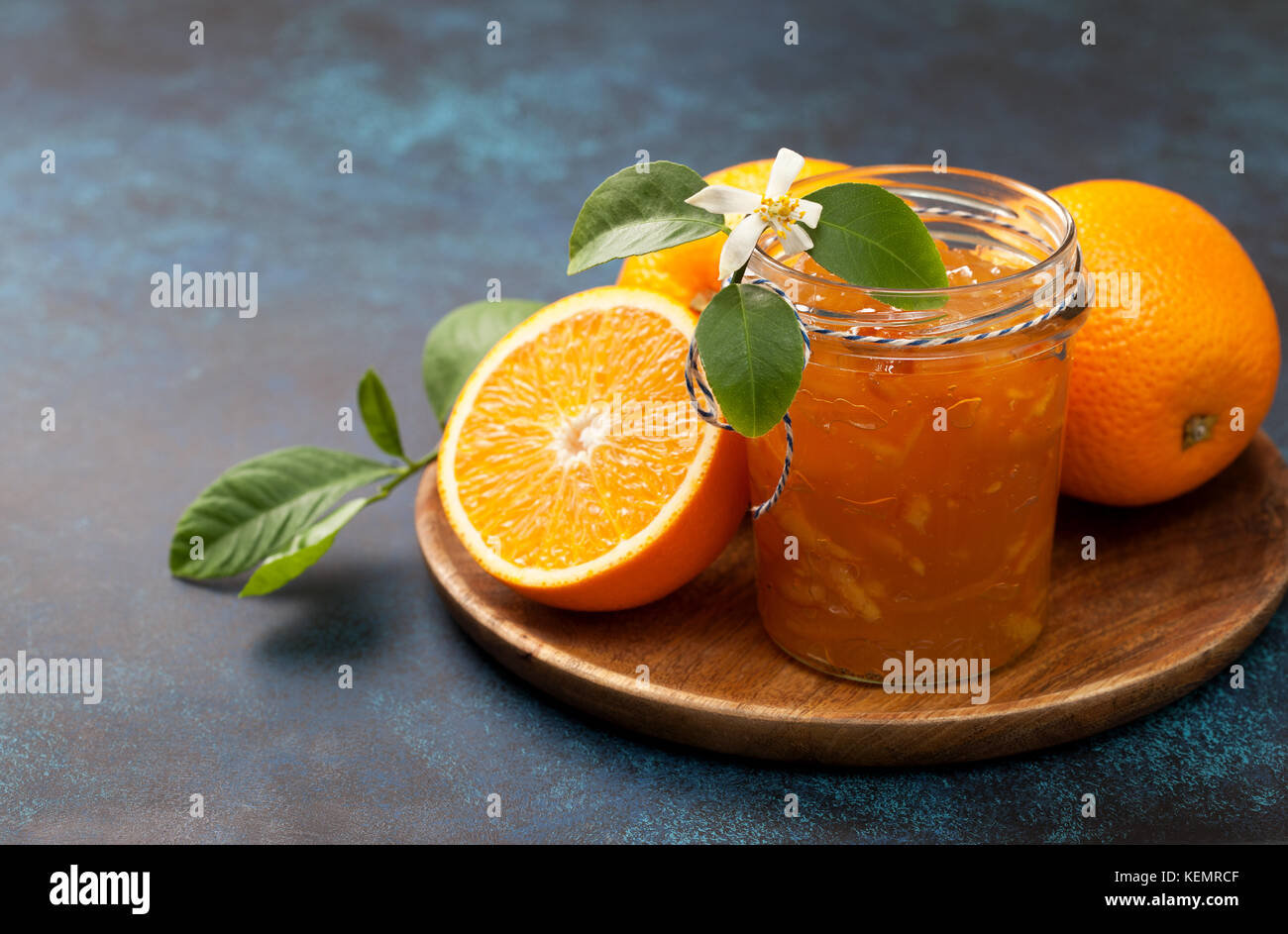 Orange inceppamento in un vasetto di vetro, arance fresche sul piatto di legno su uno sfondo blu Foto Stock