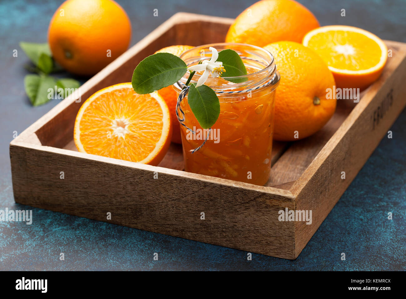 Orange inceppamento in un vasetto di vetro, arance fresche in un vassoio di legno (scatola) su uno sfondo blu Foto Stock