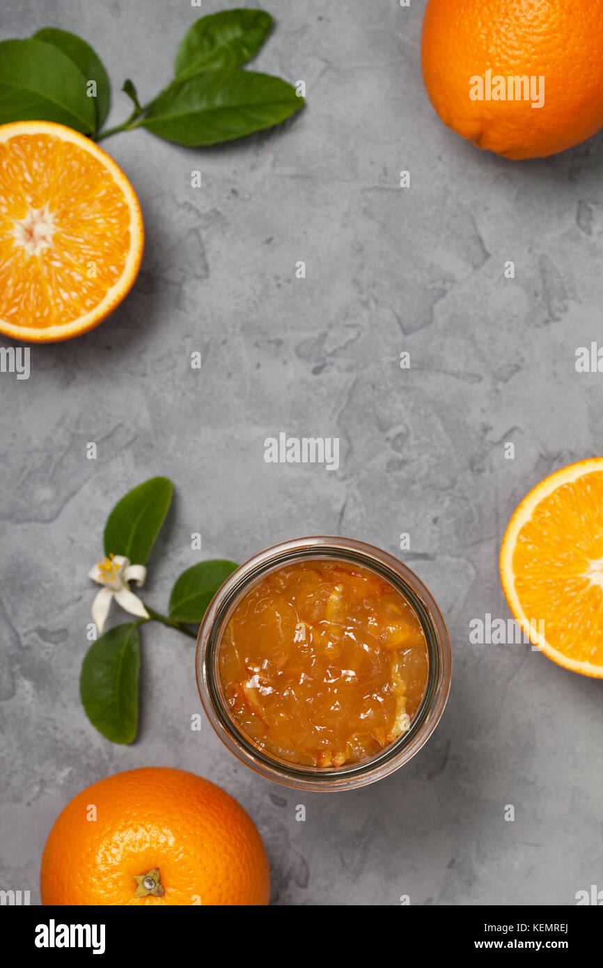 Orange inceppamento in un vasetto di vetro, arance fresche su un cemento grigio Sfondo. vista da sopra Foto Stock