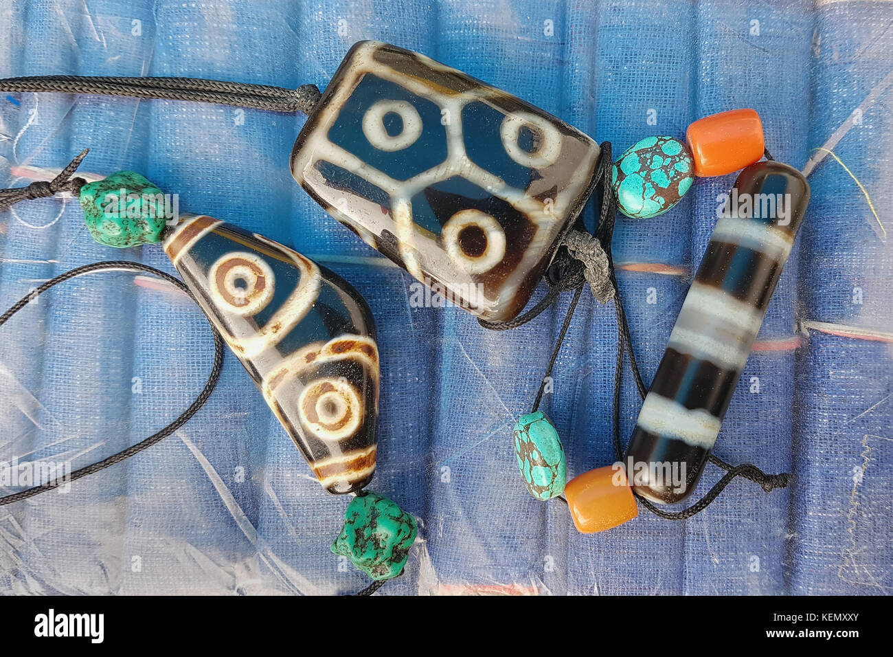 Pietre tibetano amuleti difensori Dzj, pietre infilate su funi e decorate con perline blu turchese e perle rosso corallo, talismani buddista. Foto Stock