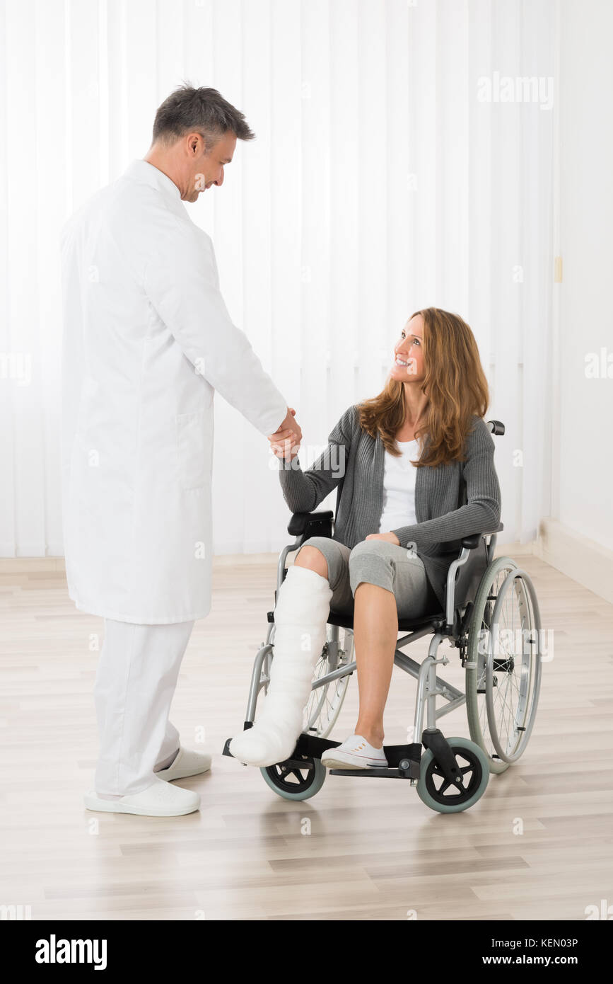 Medico maschio stringono le mani con il paziente seduto su una sedia a rotelle Foto Stock