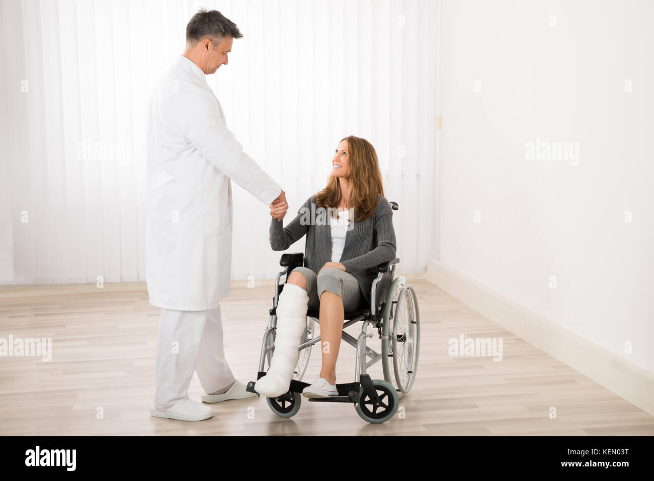Medico maschio stringono le mani con il paziente seduto su una sedia a rotelle Foto Stock