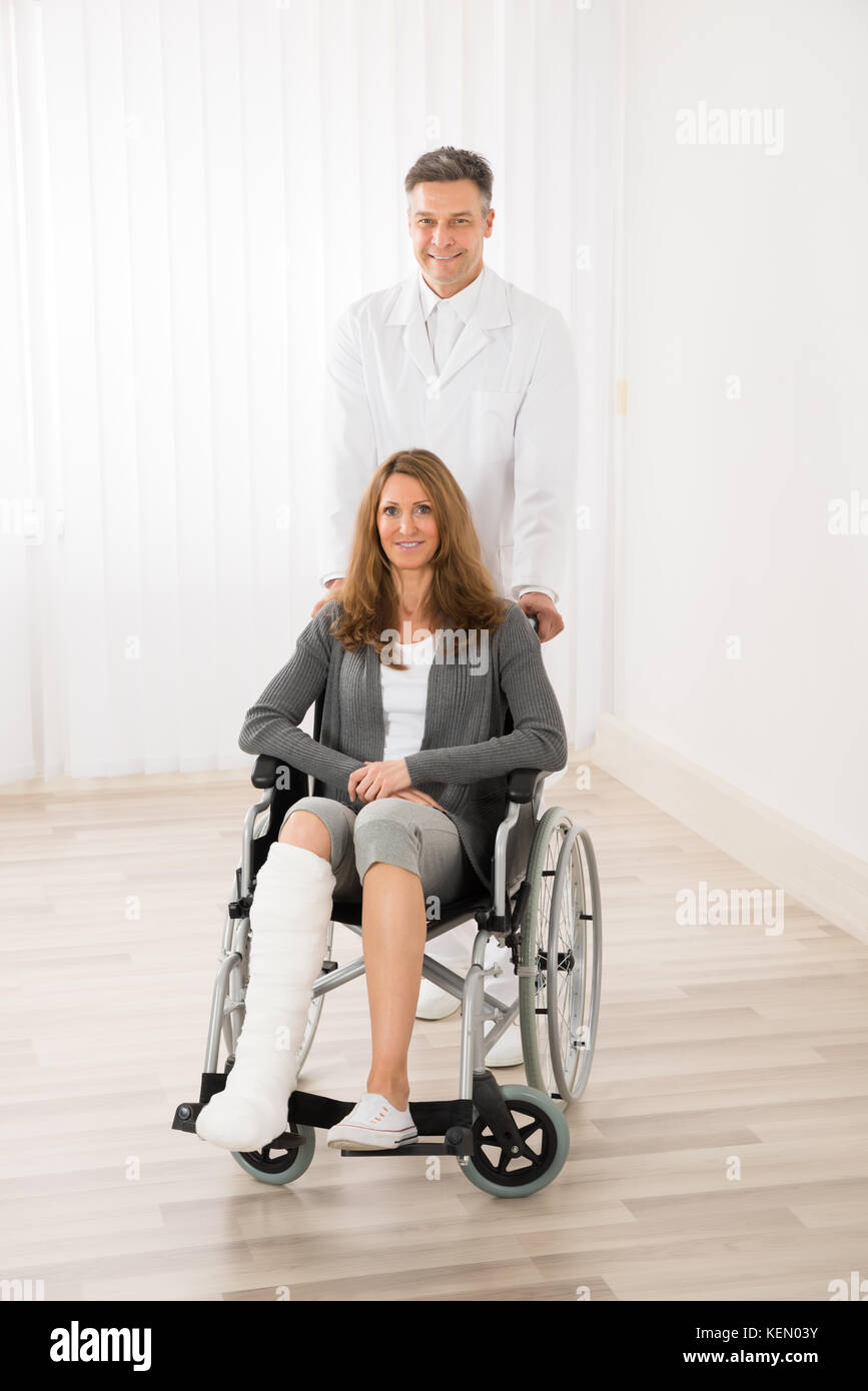 Medico maschio assistere felice donna seduta su una sedia a rotelle Foto Stock