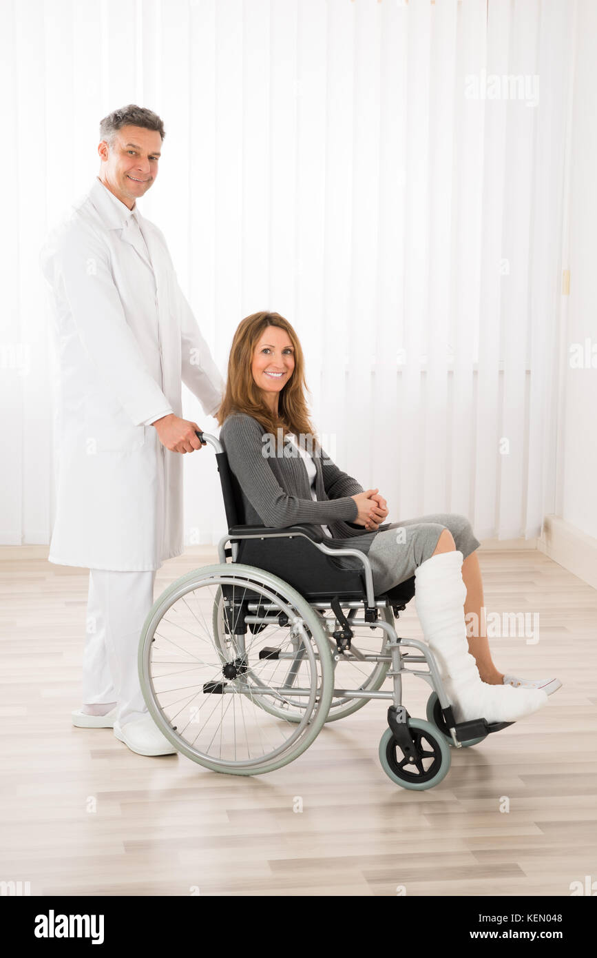 Medico maschio assistere felice donna seduta su una sedia a rotelle Foto Stock