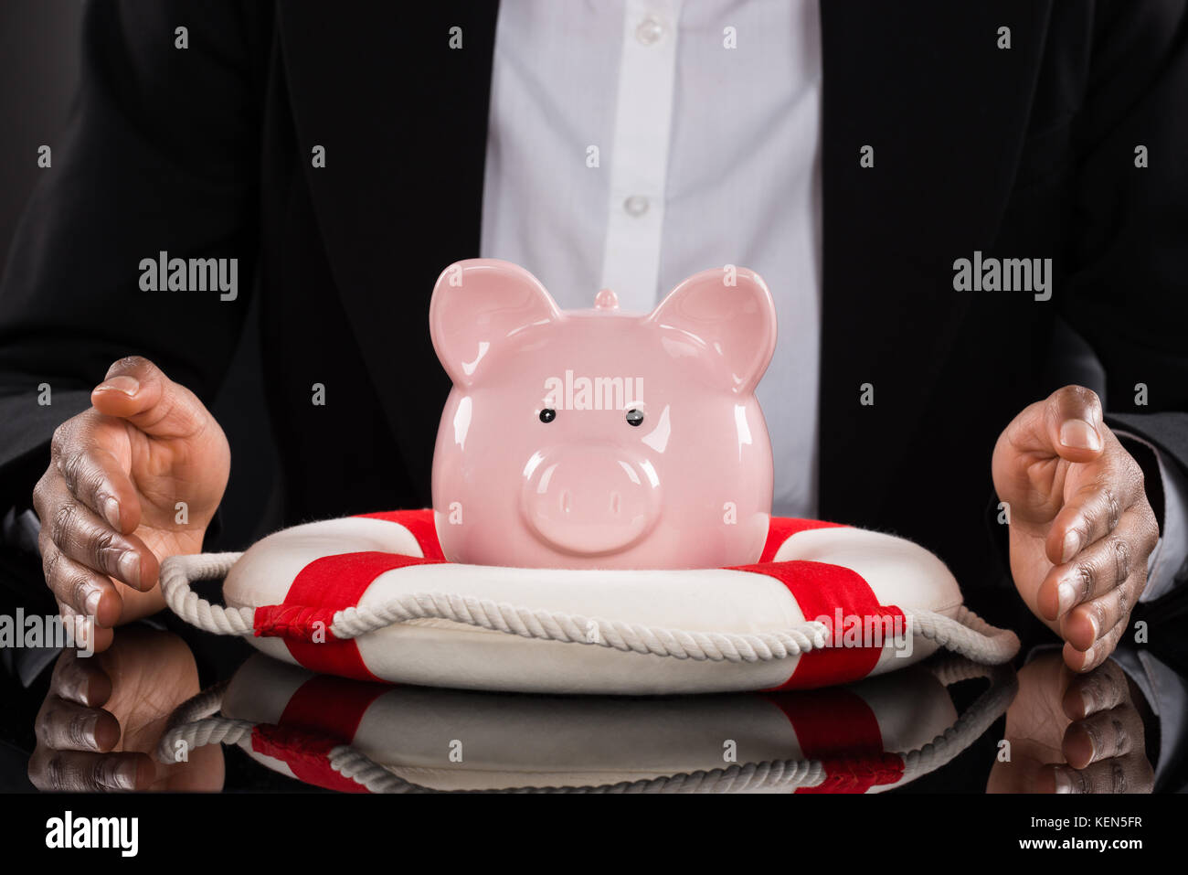 Close-up di un imprenditore di protezione mano piggybank con lifebelt sulla scrivania Foto Stock
