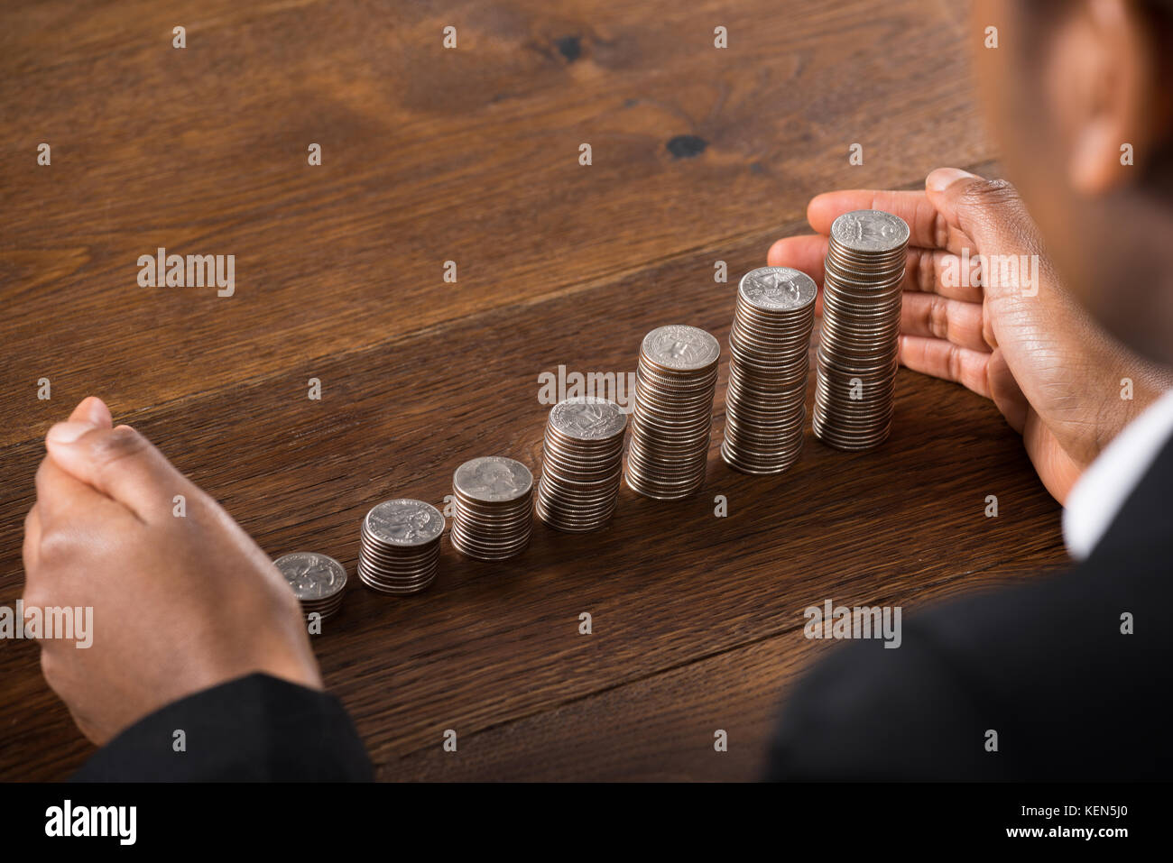 Close-up di commercianti mano proteggere le monete impilate sulla scrivania in legno Foto Stock