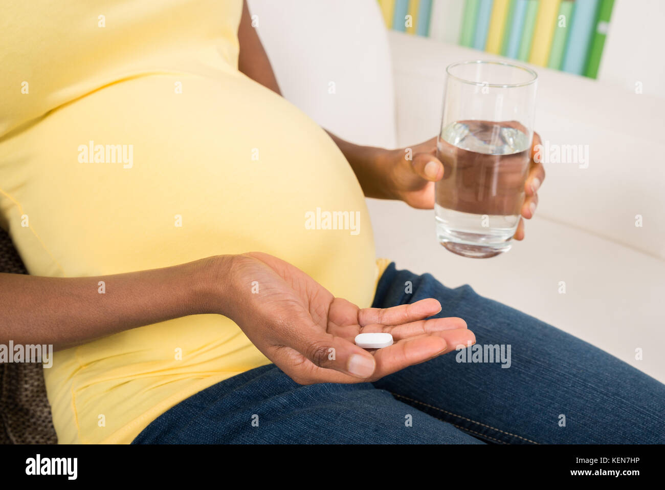 Close-up della donna incinta mano con un bicchiere di acqua e vitamina pillola Foto Stock