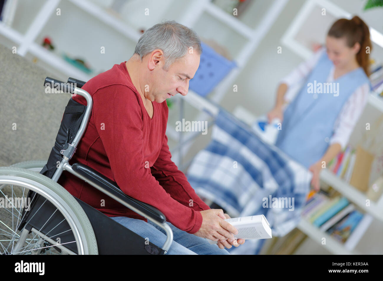 Uomo sulla sedia a rotelle e infermiere contribuendo alla stiratura Foto Stock
