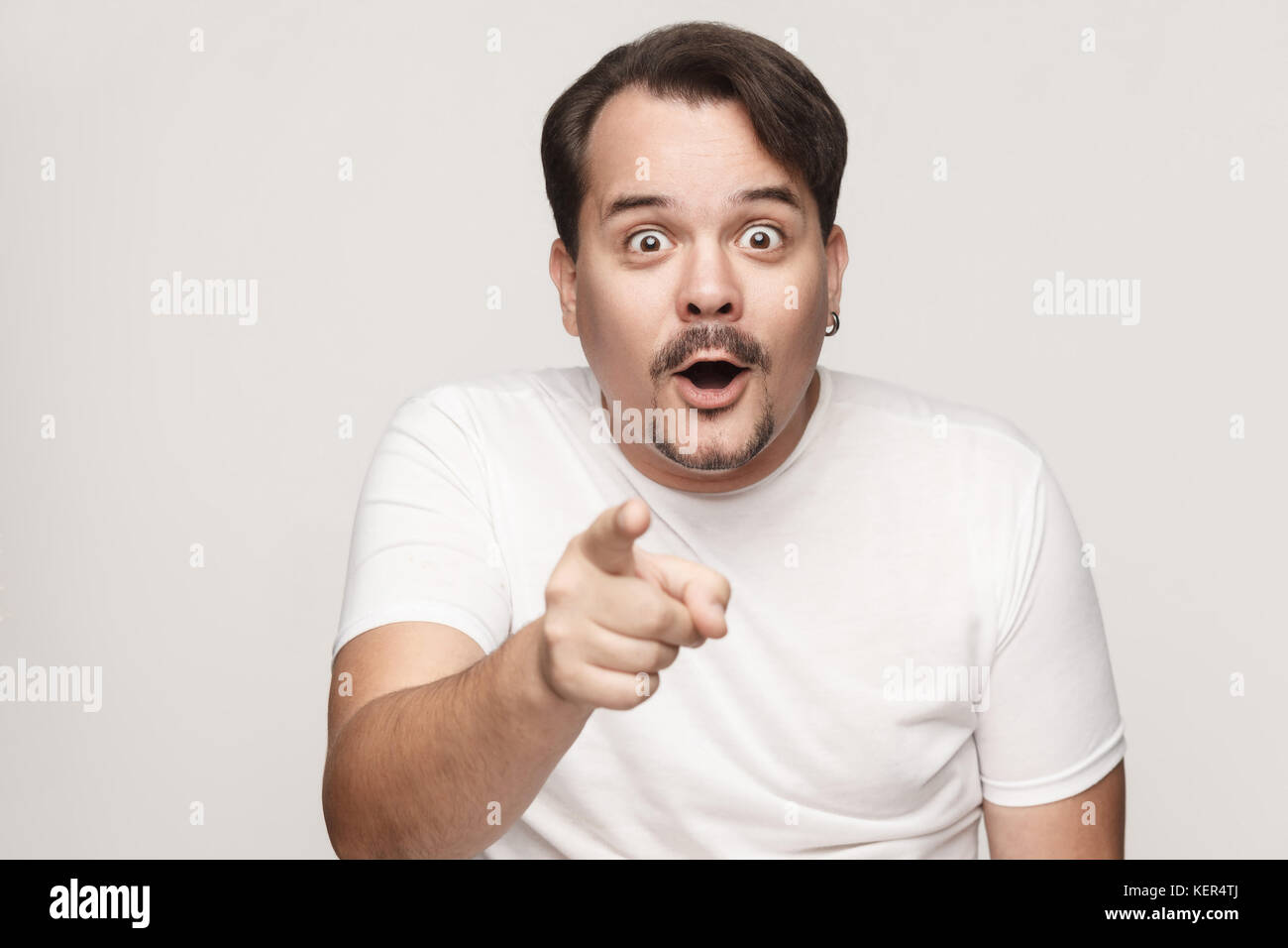 L'uomo adulto, bocche di apertura ampiamente, dopo aver stupito sconvolto guarda, puntare il dito alla telecamera. isolato studio shot su sfondo grigio Foto Stock