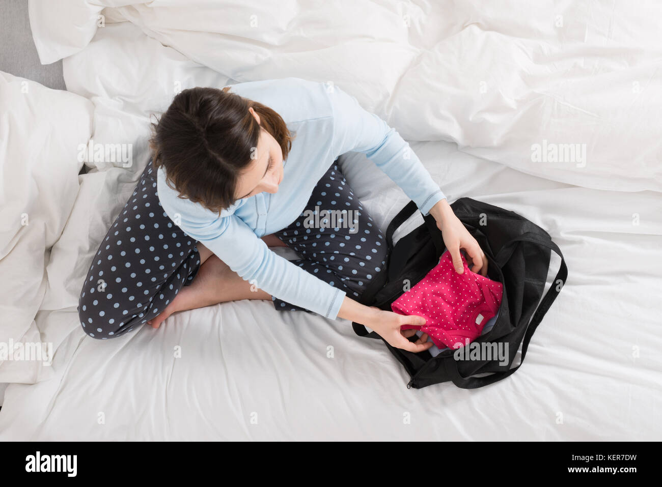 Giovane donna incinta seduta sul letto imballaggio vestiti del bambino nel sacco Foto Stock