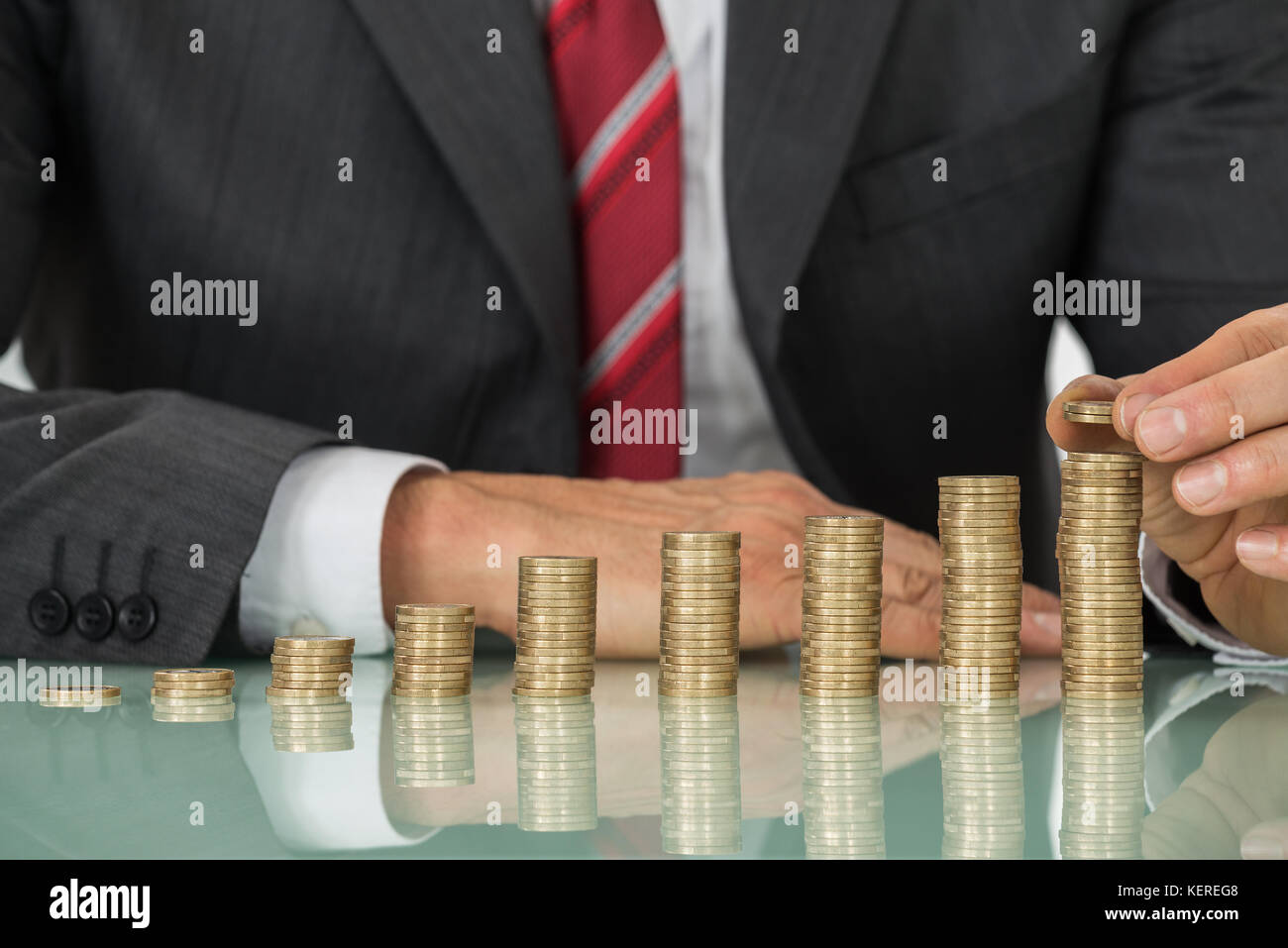 Close-up di imprenditore ponendo mano coin sulla pila di monete al banco Foto Stock