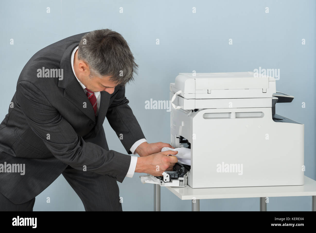 Imprenditore piegare verso il basso per rimuovere la carta bloccata nella stampante in ufficio Foto Stock