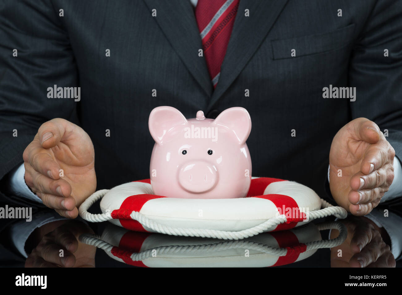 Close-up di imprenditore di protezione mano Piggybank con Lifebelt alla scrivania Foto Stock