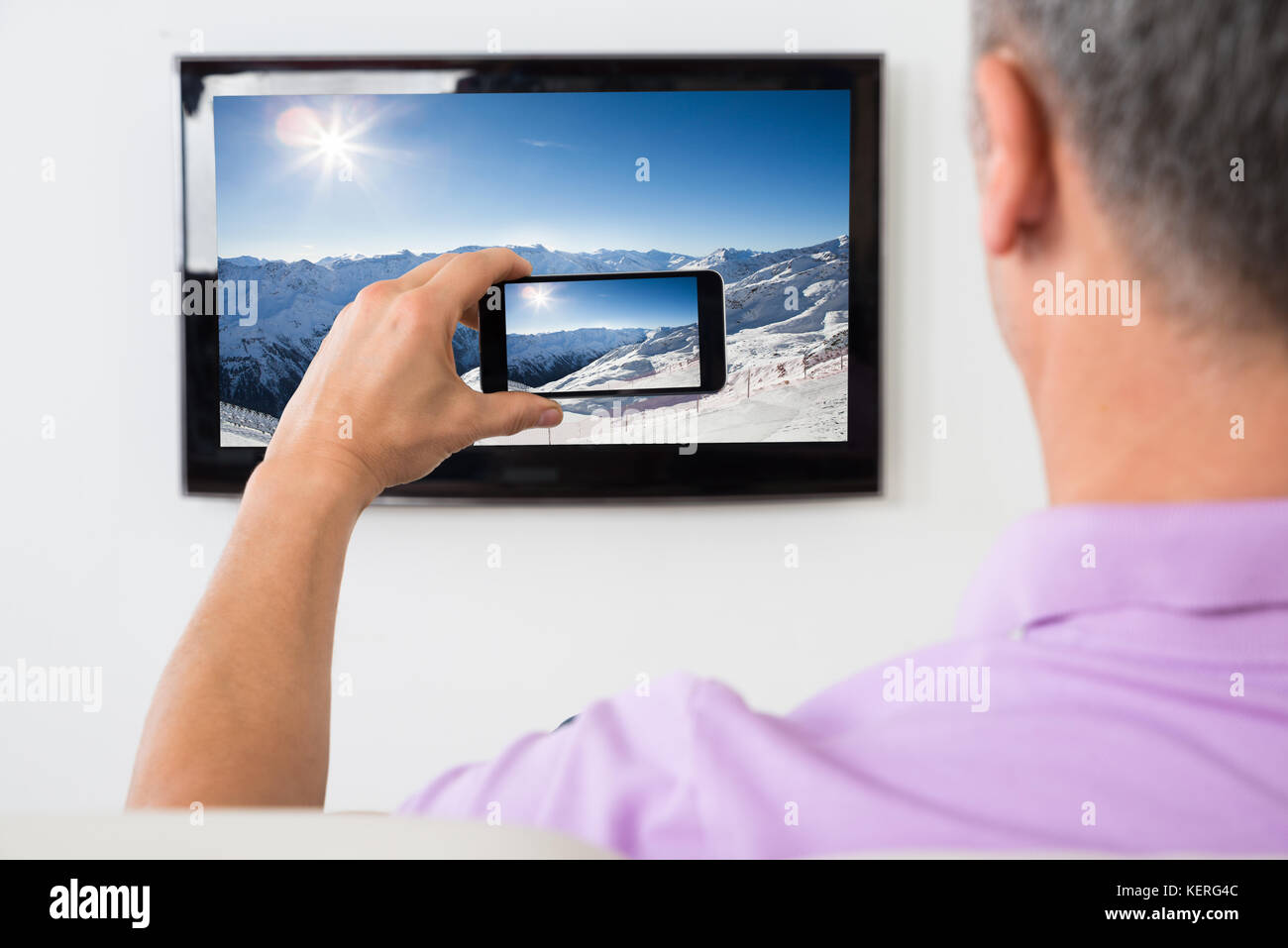 Uomo maturo con Smartphone collegato a un televisore a guardare film a casa Foto Stock