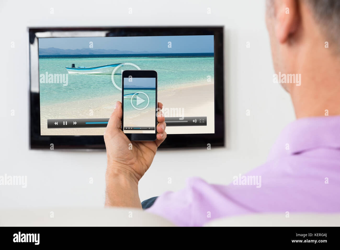 Uomo maturo con smartphone connesso a un televisore per guardare video a casa Foto Stock