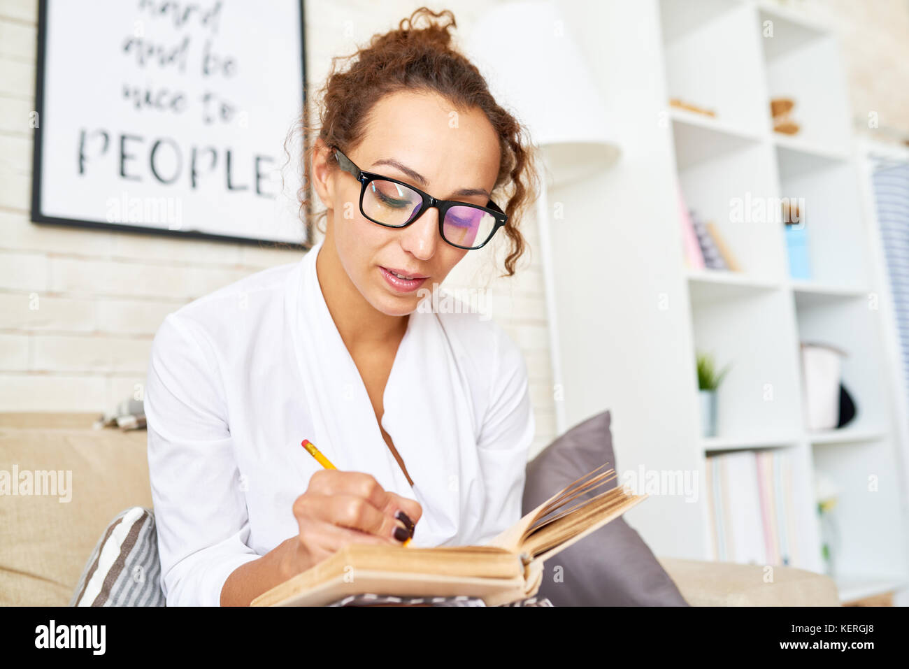 Ritratto di giovane ed elegante donna che indossa gli occhiali rendendo note in notebook mentre seduto in poltrona confortevole Foto Stock