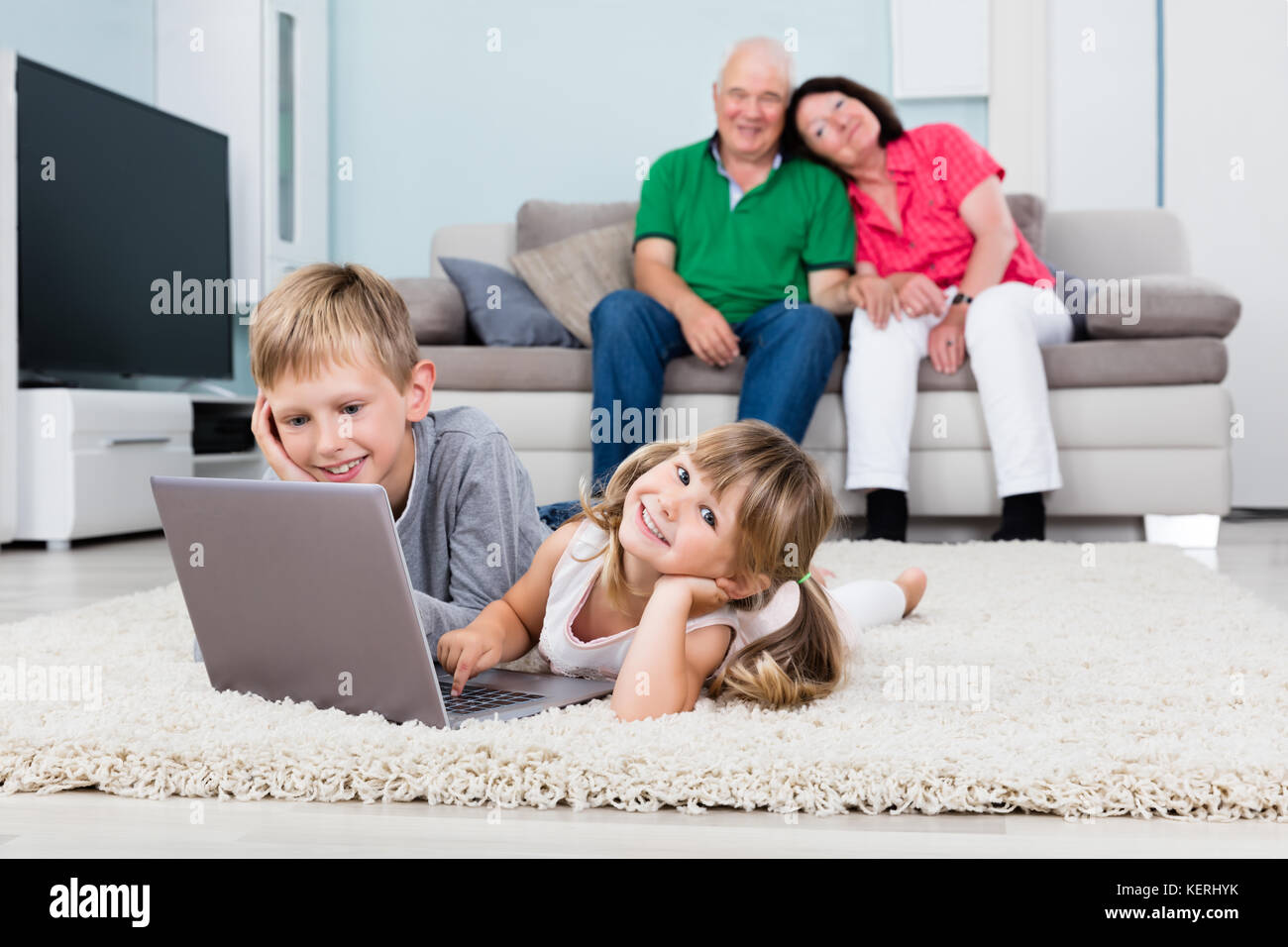 Nonni felici guardando i nipoti utilizzando computer portatile giacente su un tappeto a casa Foto Stock