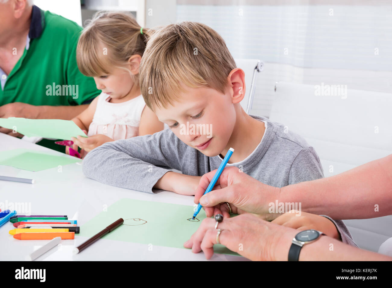 Nonni aiutando i loro nipoti per disegnare su carta colorata in casa Foto Stock