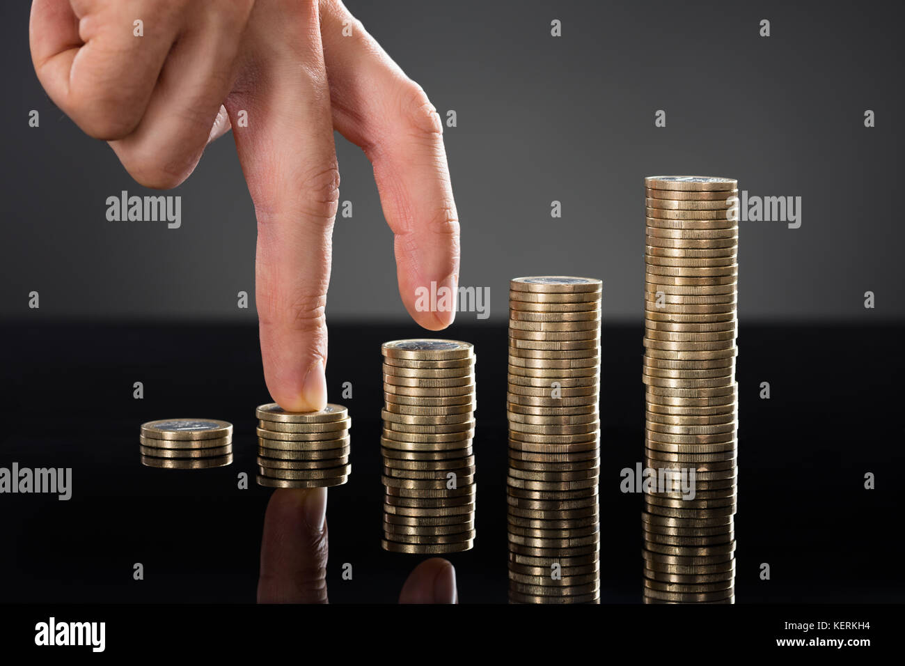 Close-up di una persona a piedi del dito fino sulla pila di monete su sfondo grigio. business il concetto di crescita Foto Stock