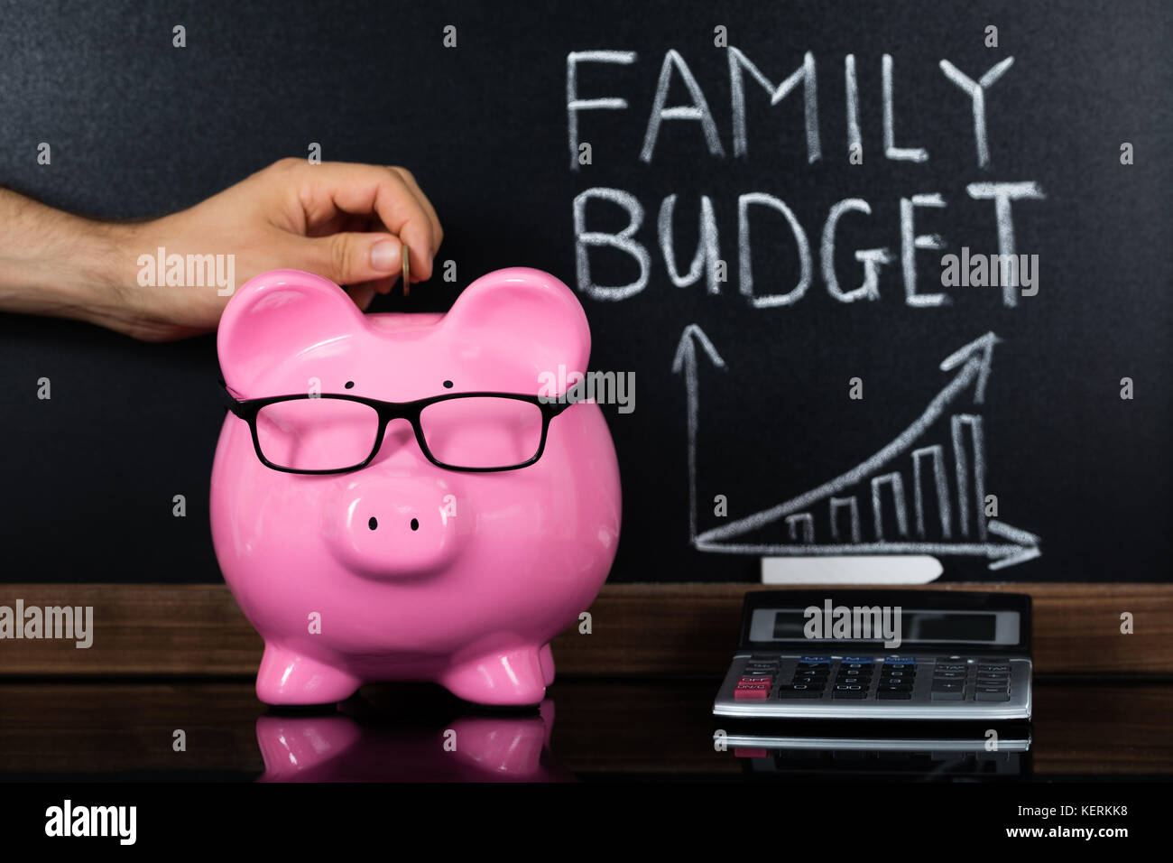 Una persona mano consentendo di risparmiare denaro in termini di piggybank per il bilancio familiare di fronte di Blackboard Foto Stock