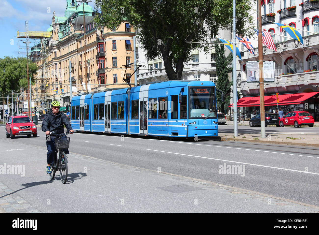 Vista della strada nel centro della città. Traffico stradale. Un moderno tram nel flusso di auto. Un anziano ciclista maschio in bicicletta sta cavalcando... Foto Stock